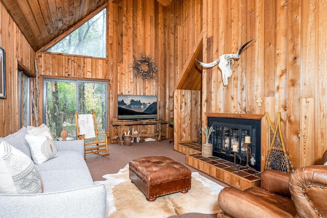 living room with high vaulted ceiling, wood walls, wood ceiling, a tiled fireplace, and carpet