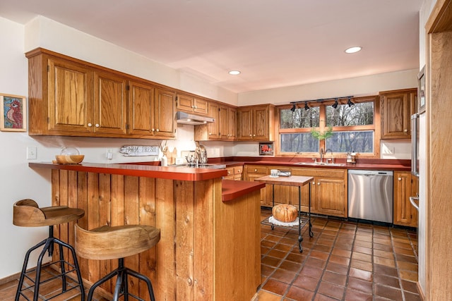 kitchen with dishwasher, brown cabinetry, and a kitchen bar