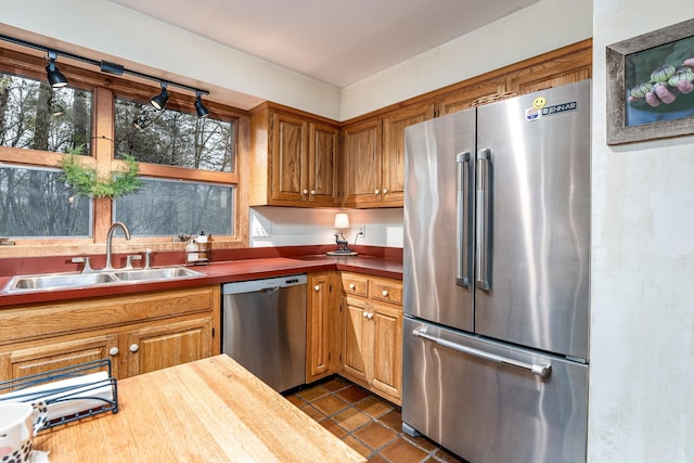 kitchen with brown cabinetry, dark tile patterned flooring, butcher block countertops, appliances with stainless steel finishes, and a sink