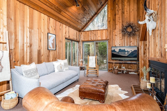 carpeted living room featuring high vaulted ceiling, wood ceiling, a fireplace with raised hearth, and wood walls