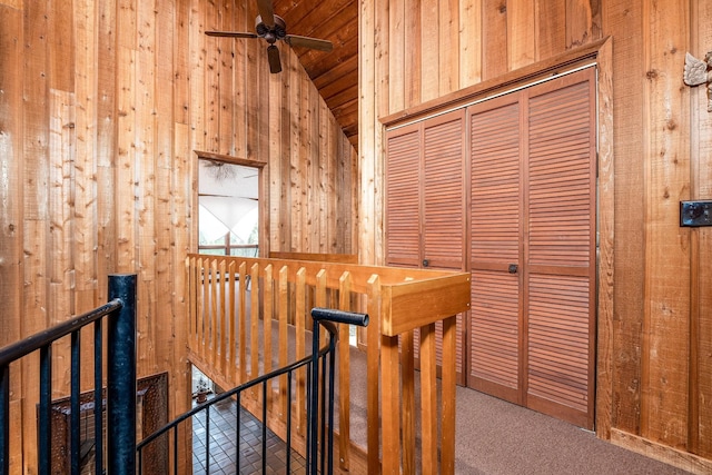 hallway featuring lofted ceiling, wooden walls, and an upstairs landing