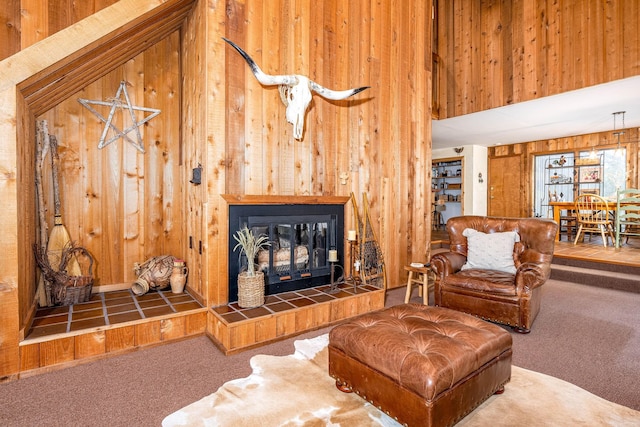 carpeted living room featuring a fireplace, a towering ceiling, and wooden walls