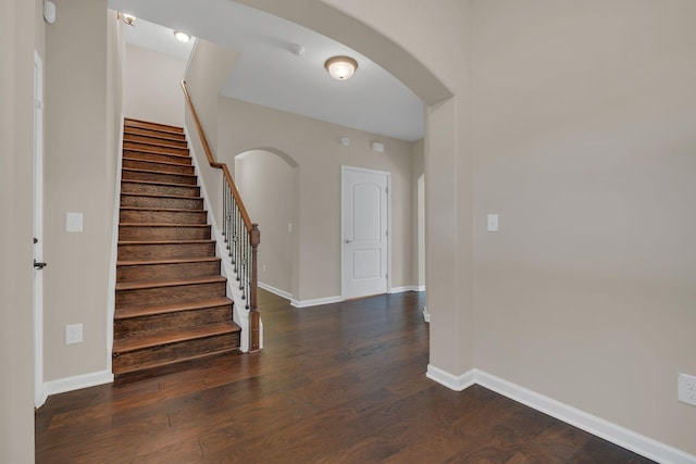 foyer with stairway, baseboards, arched walkways, and dark wood finished floors