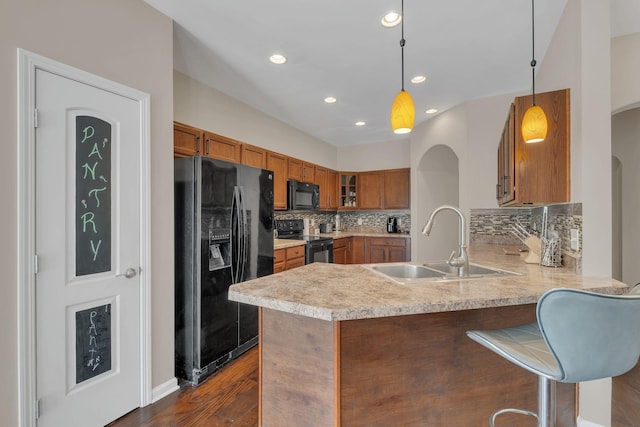 kitchen featuring brown cabinets, decorative light fixtures, light countertops, a peninsula, and black appliances