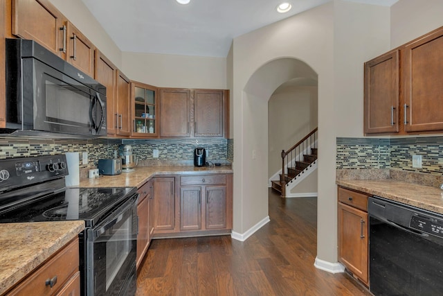 kitchen featuring arched walkways, dark wood-style flooring, glass insert cabinets, brown cabinetry, and black appliances