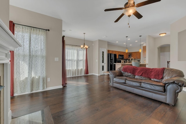 living room featuring arched walkways, recessed lighting, ceiling fan with notable chandelier, baseboards, and dark wood finished floors