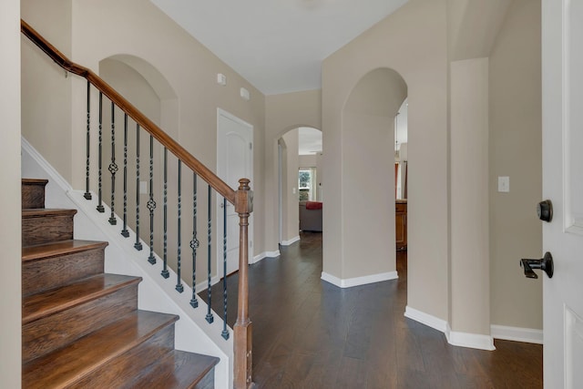 foyer entrance featuring baseboards, arched walkways, and dark wood-type flooring