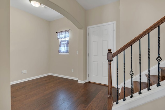 entryway featuring arched walkways, dark wood-style flooring, stairway, and baseboards