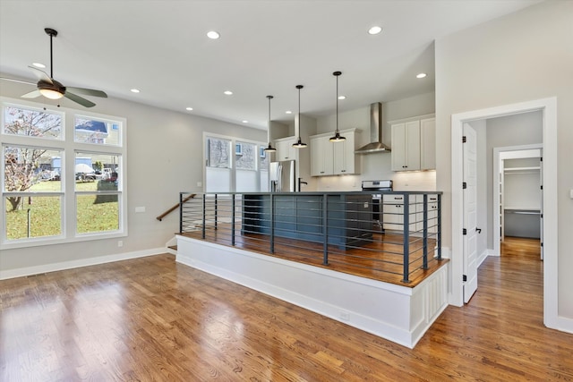 kitchen with decorative light fixtures, appliances with stainless steel finishes, white cabinetry, wall chimney range hood, and wood finished floors