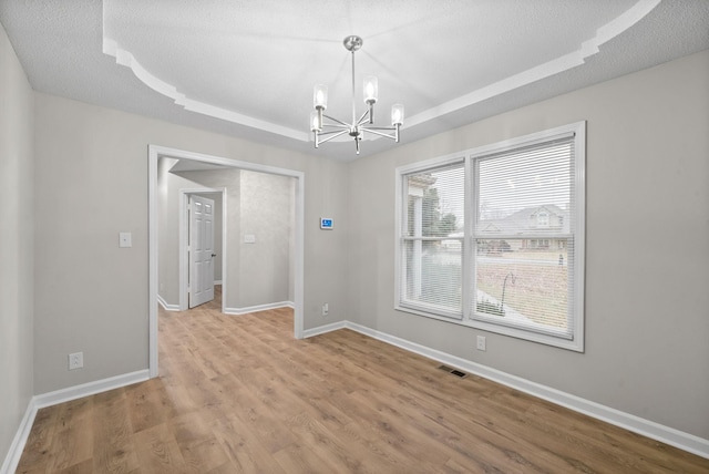 unfurnished room featuring a notable chandelier, a raised ceiling, visible vents, light wood-style floors, and baseboards