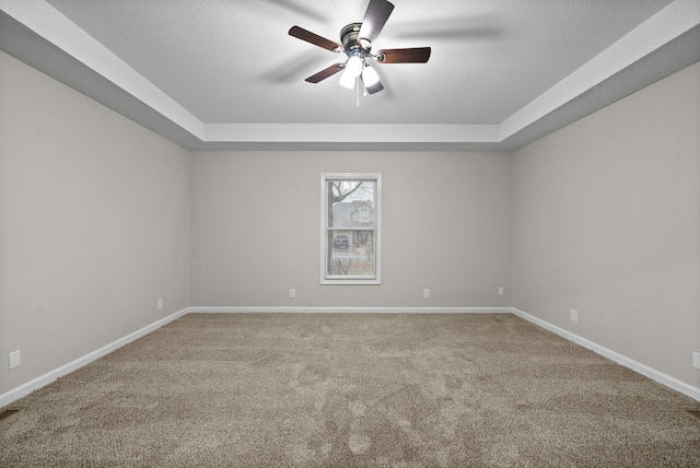 empty room with baseboards, a raised ceiling, ceiling fan, a textured ceiling, and carpet floors