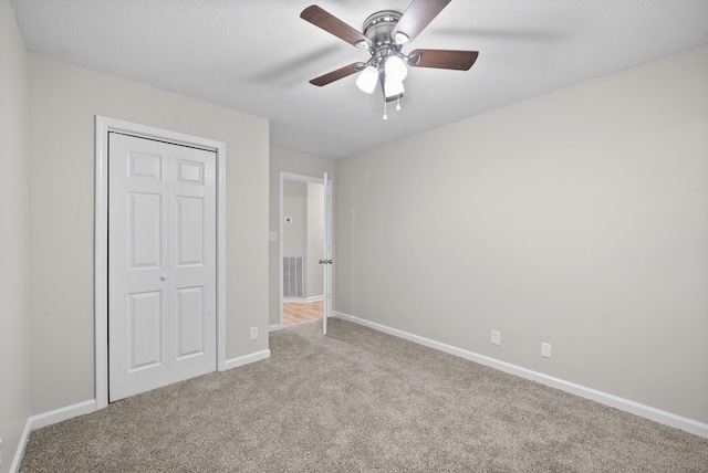 unfurnished bedroom featuring a closet, light colored carpet, visible vents, a textured ceiling, and baseboards