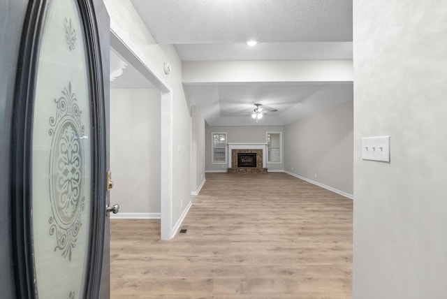 entryway featuring visible vents, a ceiling fan, a brick fireplace, light wood-type flooring, and baseboards