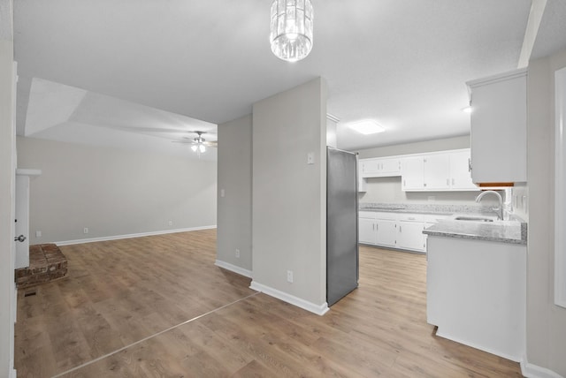 kitchen featuring a ceiling fan, open floor plan, white cabinets, a sink, and light wood-type flooring