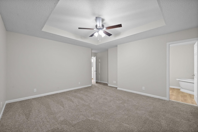 unfurnished bedroom featuring a tray ceiling, carpet, ensuite bathroom, a textured ceiling, and baseboards