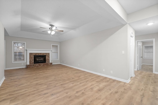 unfurnished living room with a fireplace, a raised ceiling, ceiling fan, light wood-type flooring, and baseboards