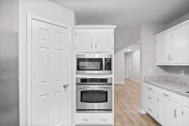 kitchen with stainless steel appliances, white cabinets, a textured ceiling, light wood-type flooring, and baseboards