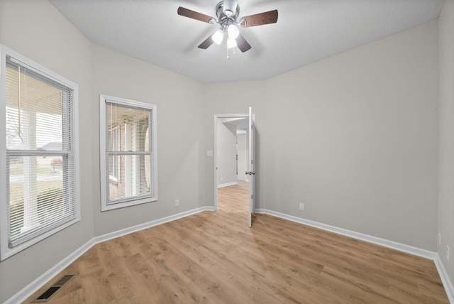 spare room with light wood-type flooring, baseboards, visible vents, and a ceiling fan