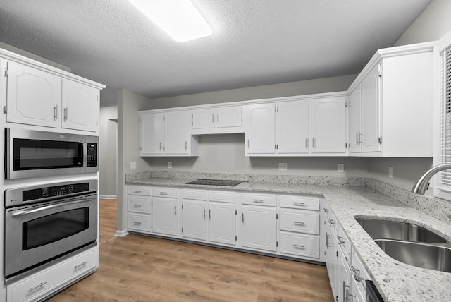 kitchen featuring light stone counters, wood finished floors, a sink, white cabinetry, and appliances with stainless steel finishes