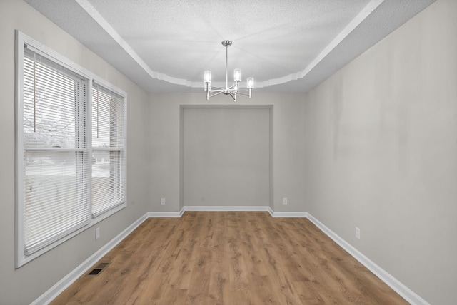 unfurnished dining area with a tray ceiling, visible vents, a textured ceiling, and baseboards