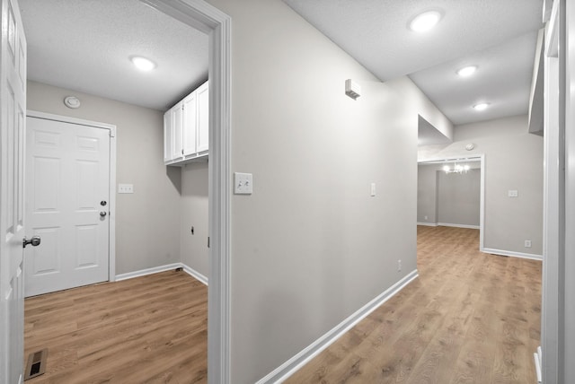 corridor featuring light wood finished floors, visible vents, and a textured ceiling