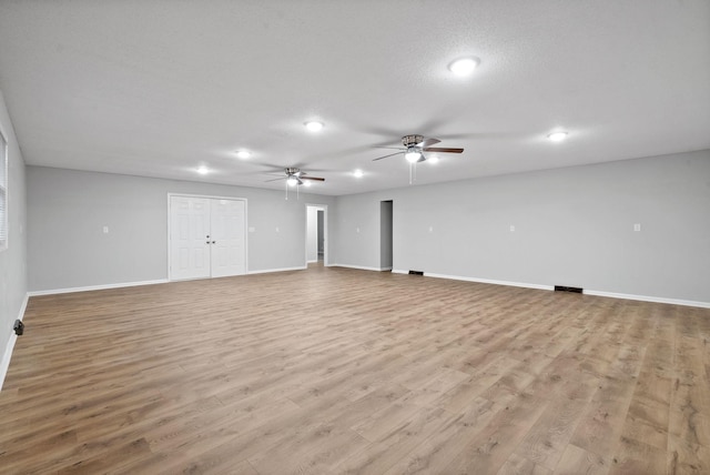 empty room with a textured ceiling, light wood finished floors, a ceiling fan, and baseboards