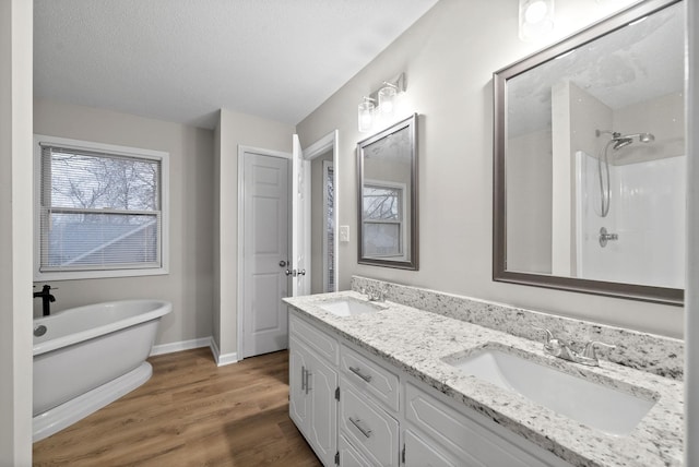 full bathroom featuring a soaking tub, a textured ceiling, a sink, and wood finished floors