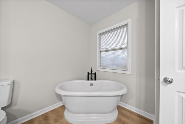 full bathroom with a freestanding bath, wood finished floors, toilet, and baseboards