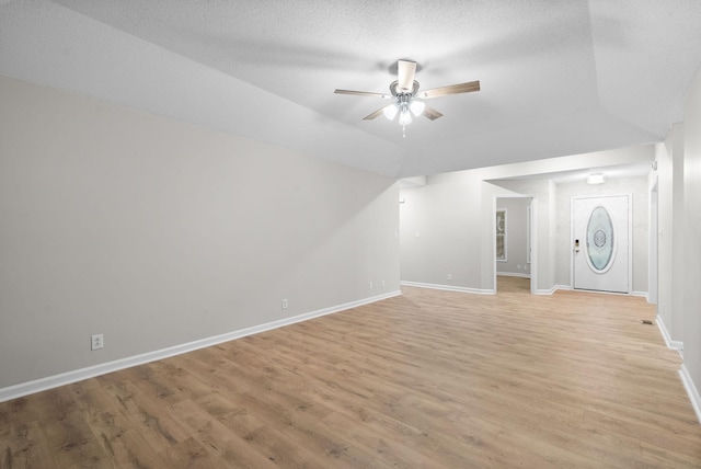 interior space with vaulted ceiling, ceiling fan, a textured ceiling, light wood-type flooring, and baseboards