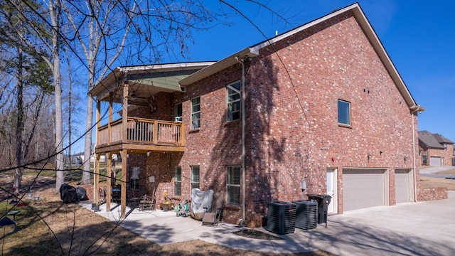 back of property with a garage, brick siding, a balcony, and central air condition unit