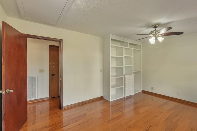 unfurnished bedroom featuring visible vents, attic access, a textured ceiling, wood finished floors, and baseboards