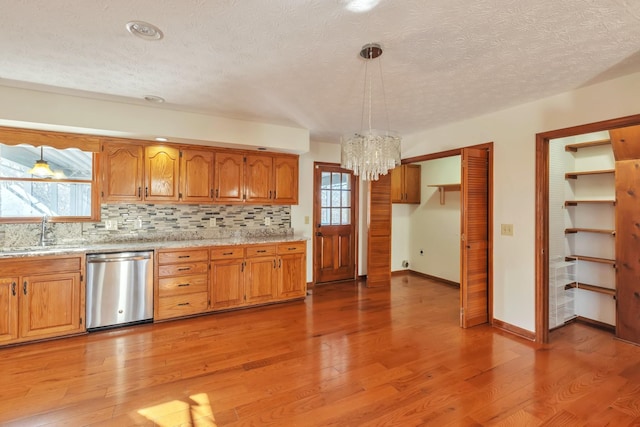 kitchen with brown cabinetry, light countertops, stainless steel dishwasher, pendant lighting, and a sink