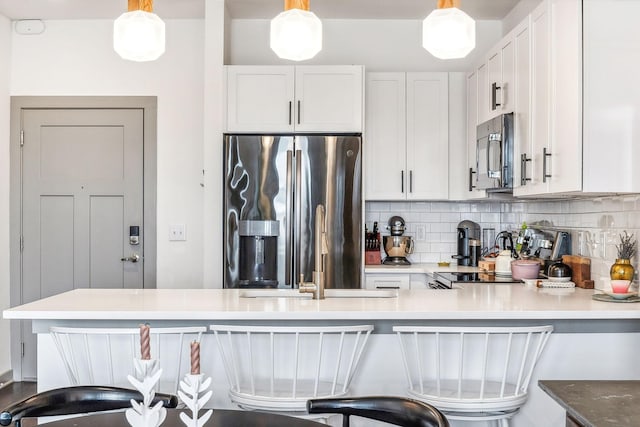 kitchen with hanging light fixtures, appliances with stainless steel finishes, a kitchen bar, and white cabinets