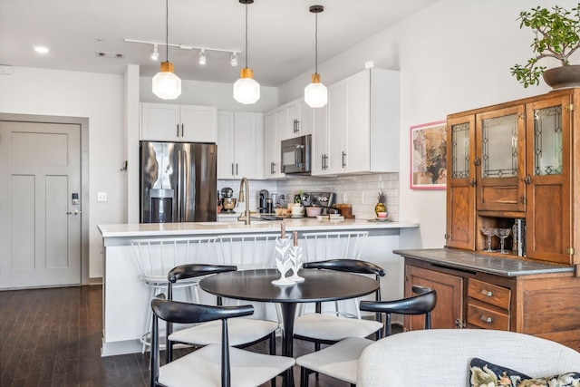 kitchen with white cabinets, light countertops, tasteful backsplash, stainless steel fridge, and decorative light fixtures