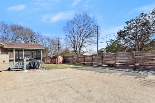 view of yard featuring a sunroom, a fenced backyard, an outdoor structure, and a storage unit