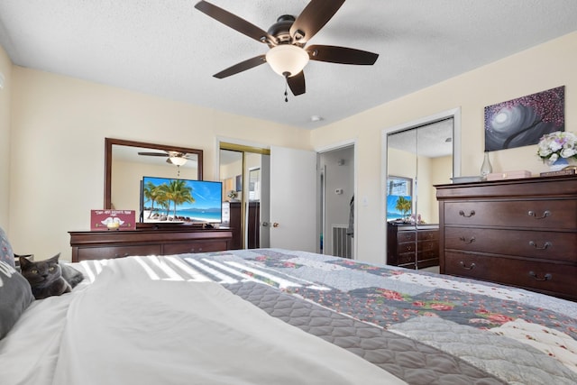 bedroom featuring a textured ceiling, a ceiling fan, and multiple closets