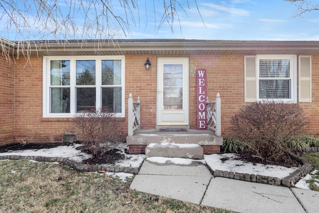 snow covered property entrance featuring brick siding