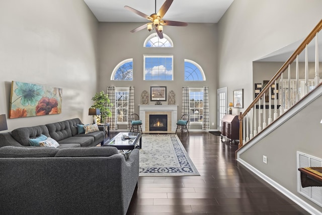 living room with a tile fireplace, a ceiling fan, baseboards, stairs, and dark wood-style floors