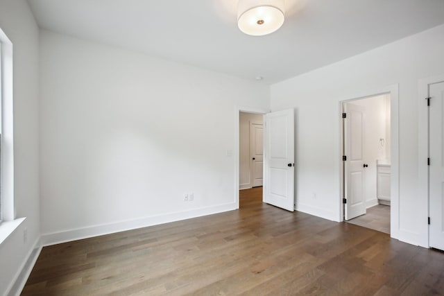 unfurnished bedroom with ensuite bathroom, baseboards, and wood finished floors