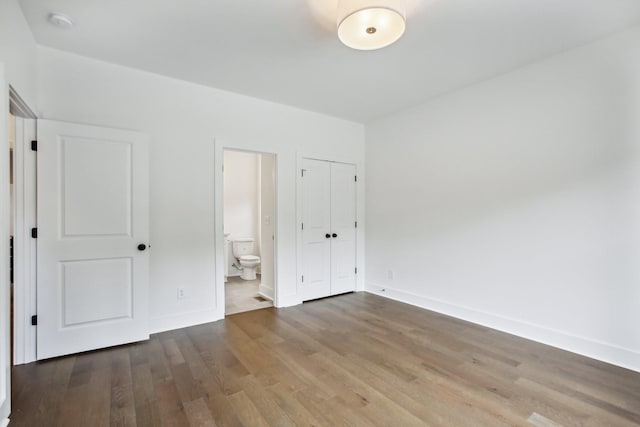 unfurnished bedroom featuring a closet, ensuite bath, baseboards, and wood finished floors