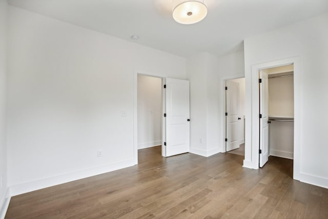 unfurnished bedroom featuring a closet, baseboards, a walk in closet, and wood finished floors