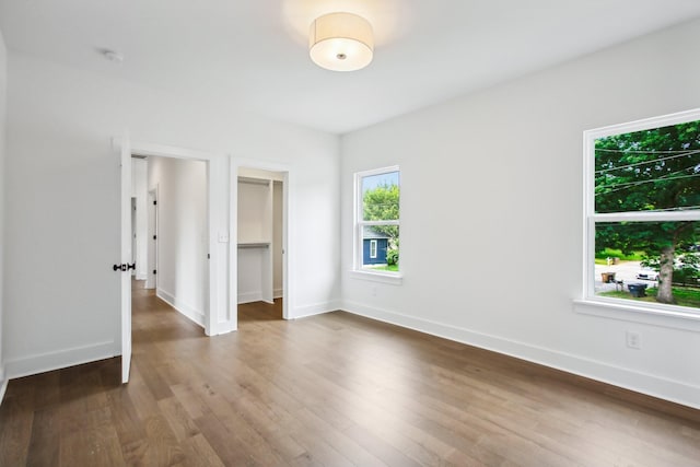 unfurnished bedroom featuring dark wood-style floors, a spacious closet, a closet, and baseboards