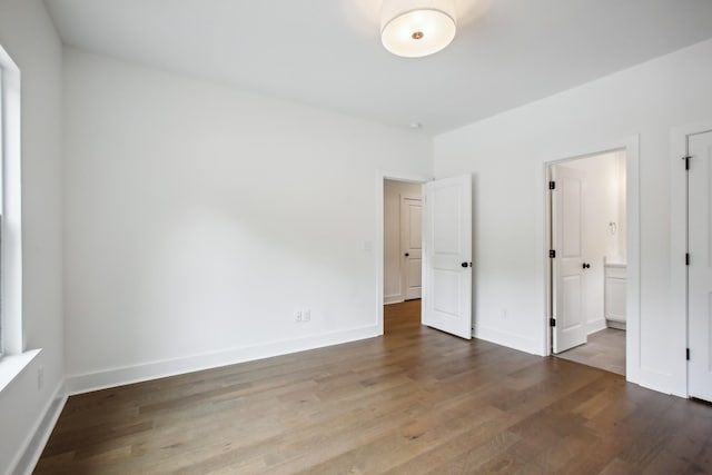 unfurnished bedroom featuring ensuite bath, baseboards, and wood finished floors