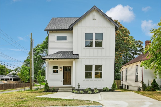 modern farmhouse featuring board and batten siding, a shingled roof, a front lawn, and fence