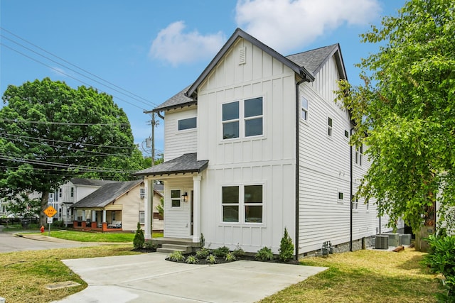 modern inspired farmhouse with board and batten siding, a front yard, a shingled roof, and central AC unit