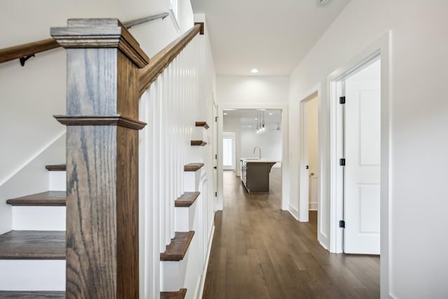 hallway featuring stairs, dark wood-style flooring, a sink, and recessed lighting