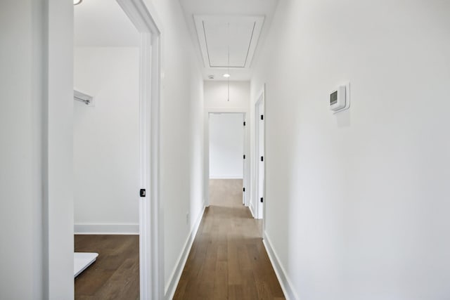 hallway featuring attic access, baseboards, and wood finished floors