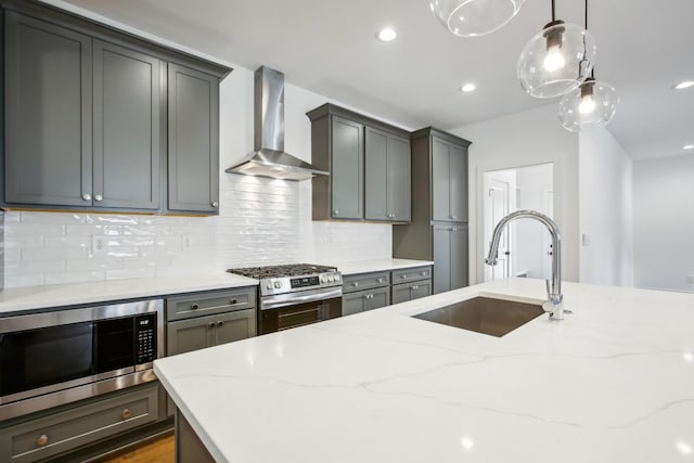 kitchen with a sink, wall chimney range hood, appliances with stainless steel finishes, light stone countertops, and decorative light fixtures