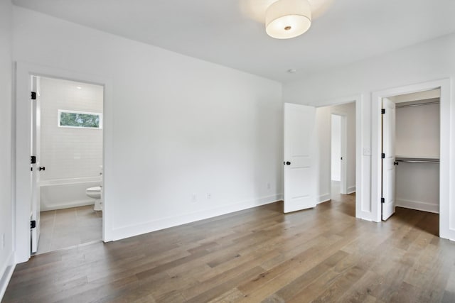 unfurnished bedroom with a closet, baseboards, wood finished floors, and ensuite bathroom