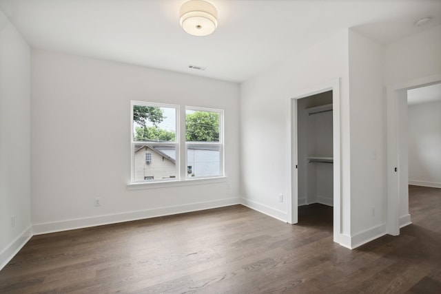 unfurnished bedroom featuring a spacious closet, dark wood-style flooring, visible vents, and baseboards